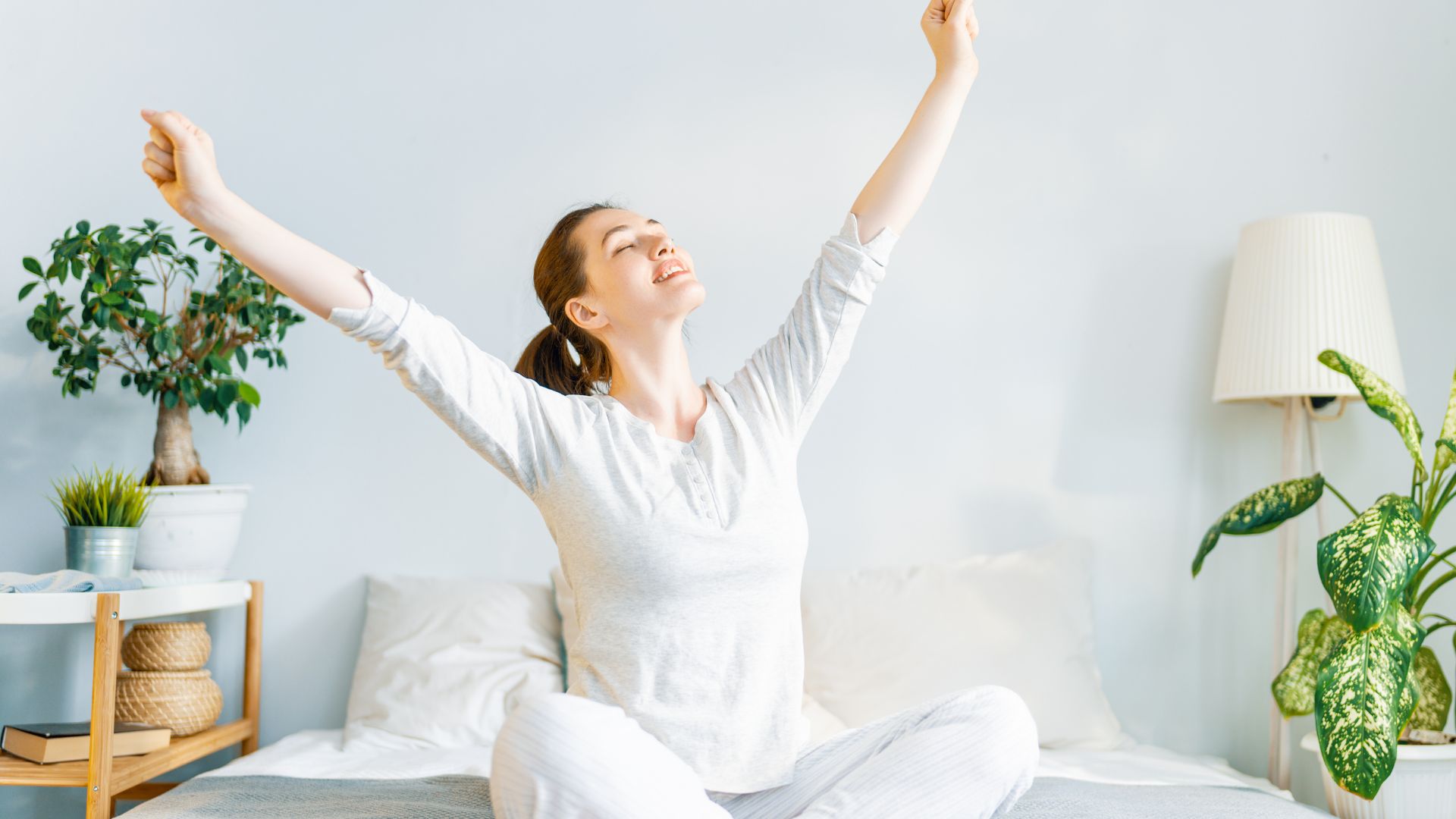 A woman sitting on a bed raising her arms in the air